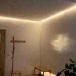 Entrée sombre sans fenêtre éclairée par des appliques murales et des LED chaudes, créant une ambiance accueillante