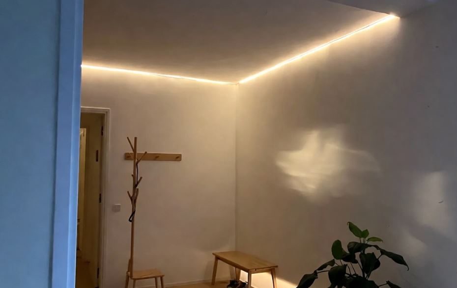 Entrée sombre sans fenêtre éclairée par des appliques murales et des LED chaudes, créant une ambiance accueillante