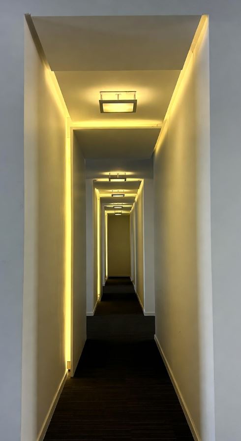 Couloir long et étroit éclairé par une lumière indirecte chaude intégrée en plafond et le long des murs